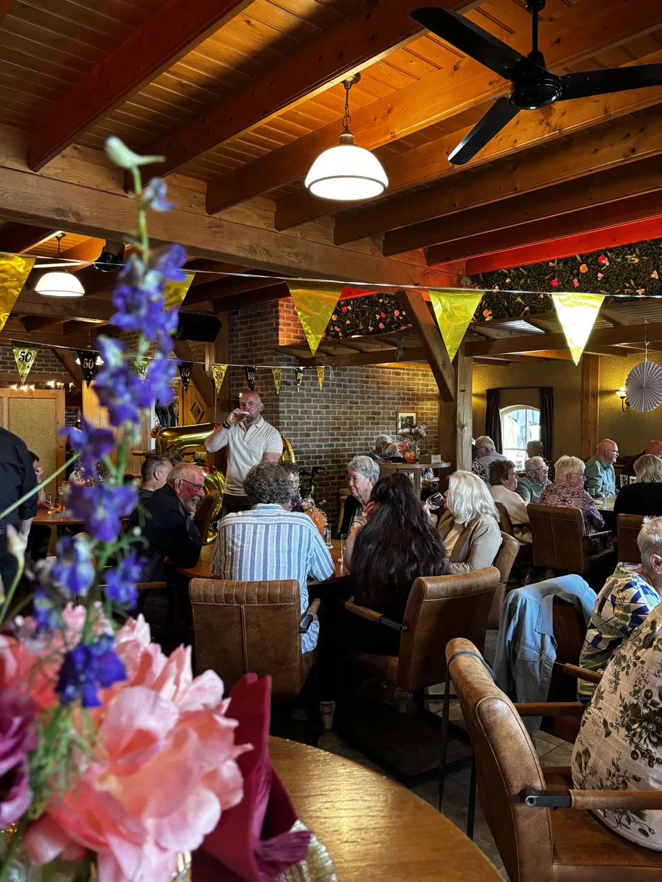 Gezellige volle zaal met 50e verjaardag versiering en bloemen op de voorgrond