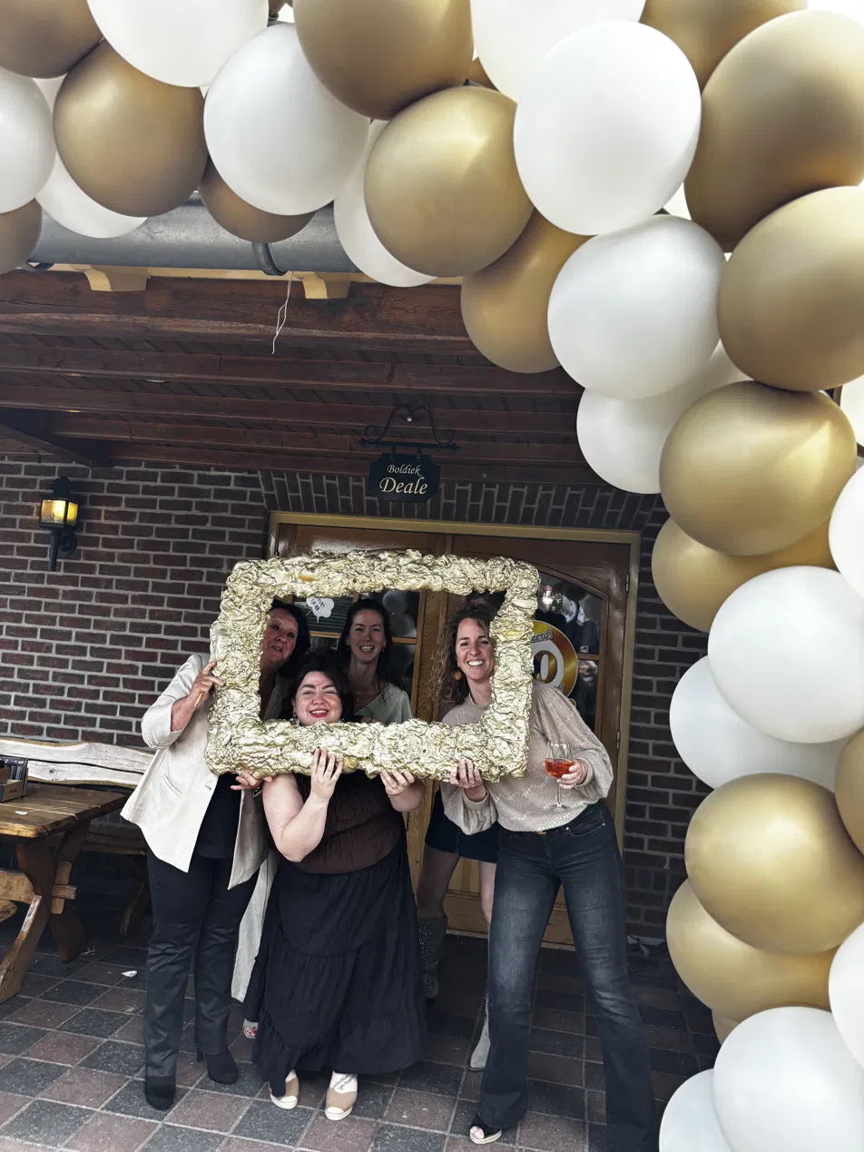 Vier vrouwen met gouden fotolijst onder wit-gouden ballonnenboog bij de ingang van De Boldiek