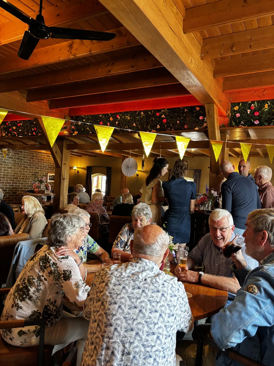Volle zaal met gele slingers en vlaggetjes tijdens een feest of jubileum op De Boldiek