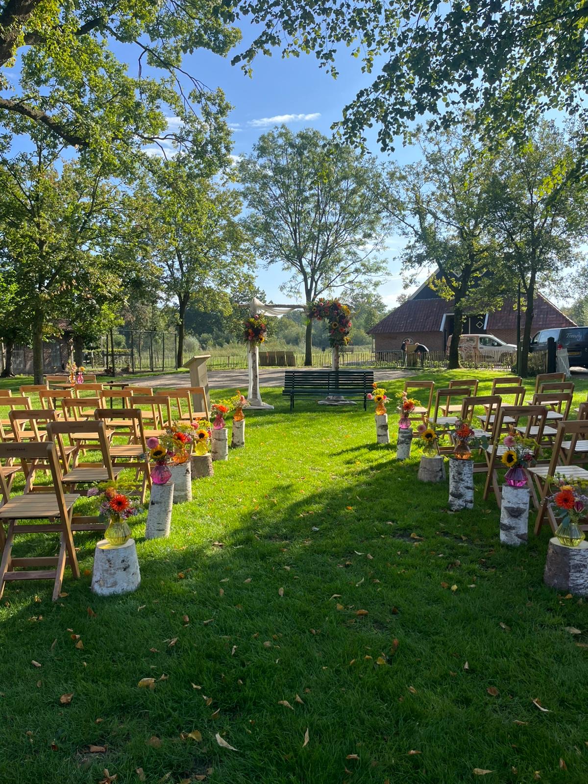 Buitenceremonie met bloemenboog en houten klapstoelen op het gras bij De Boldiek