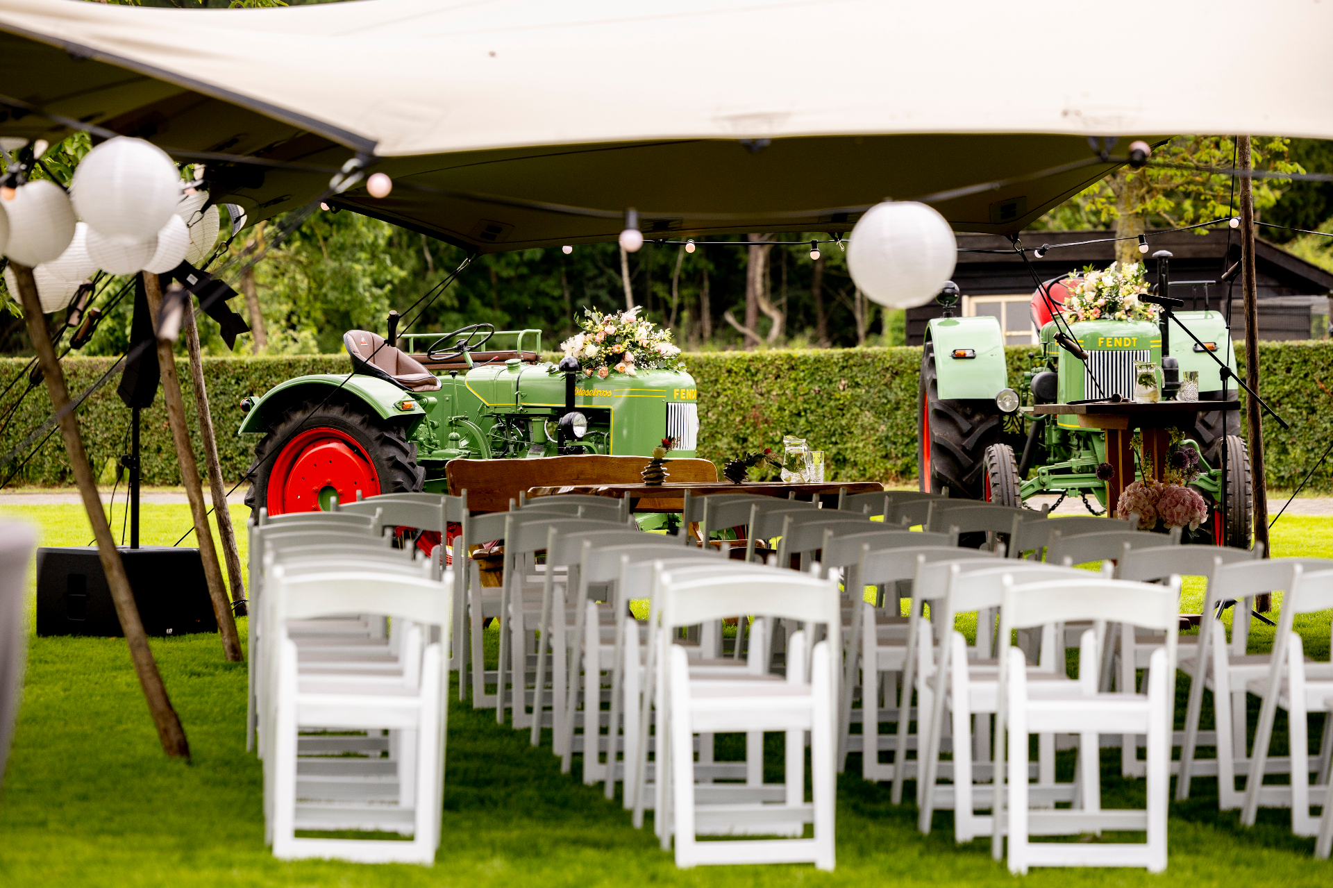 Buitenceremonie onder stretchtent met vintage Fendt tractoren en witte klapstoelen
